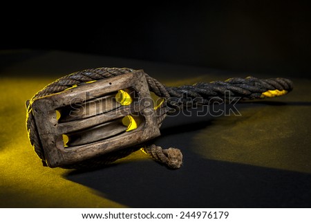 Ancient marine wood pulley with rope with grazing yellow light and black background