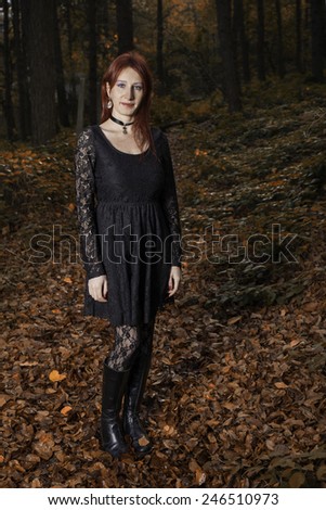 Beautiful white girl in gothic clothes stand in a forest with red autumn colors