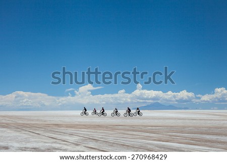 cyclists group riding the desert of salt, in salares de Uyuni, Bolivia. White clouds in the horizon, under a blue sky background