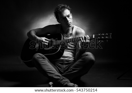Young caucasian man play a acoustic guitar. Black and white picture, low key studio portrait