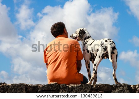Dalmatian dog and man in orange shirt against blue sky with white clouds