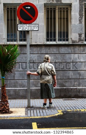 Old woman standing next to a palm tree and holding on to a street sign