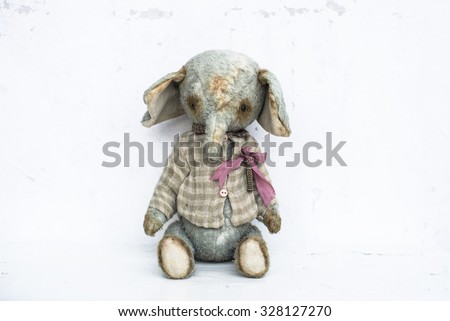Light blue battered vintage toy elephant in checkered shirt with pink bow pinned to it