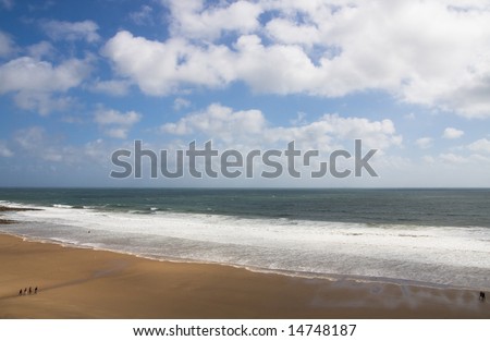 Ocean waves hitting the yellow sand under the blue and white sky