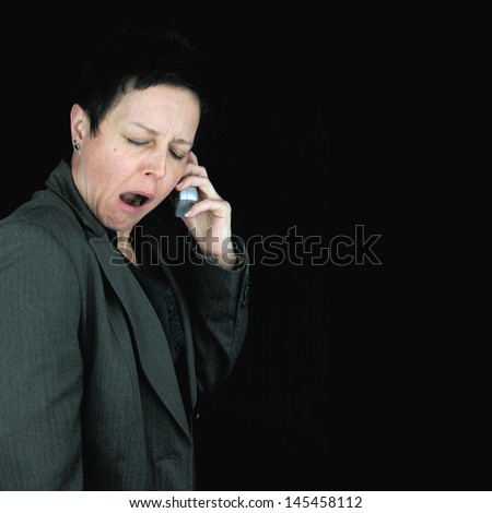 bored, tired businesswoman yawning during telephone conversation, against black background
