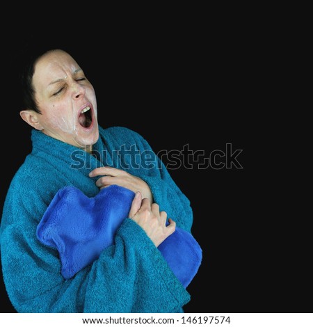 tired yawning woman, ready for bed in dressing gown, holding hot water bottle