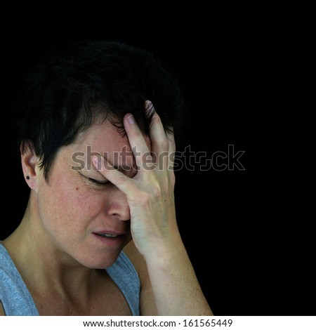 Distressed woman holding head in pain. Isolated portrait on black background.