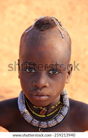 EPUPA, NAMIBIA- MAY 12, 2014: Unidentified Himba child. Himba children show their traditional clothing, jewelry and headdress. The age and social status  can be seen in their hairstyle and jewelry.