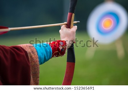 young woman in ancient clothes archery
