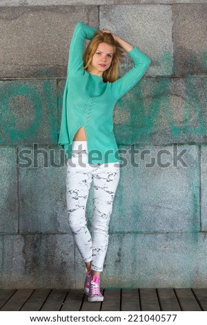 Beautiful girl in a green blouse and pink gumshoes on a concrete wall background