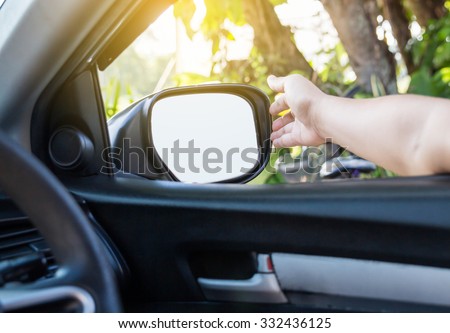 Hand adjusting side rear-view mirror.