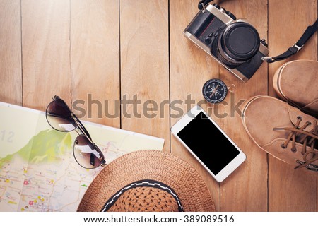 Preparation for travel,trip vacation, tourism mock up of cell phone,road map,compass,camera,hat,shoes,sunglasses on wooden table.