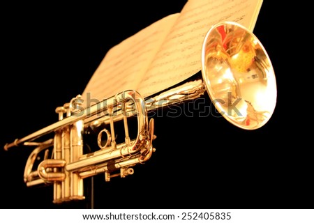 Golden trumpet on black background with sheet music as seen from the front and low.