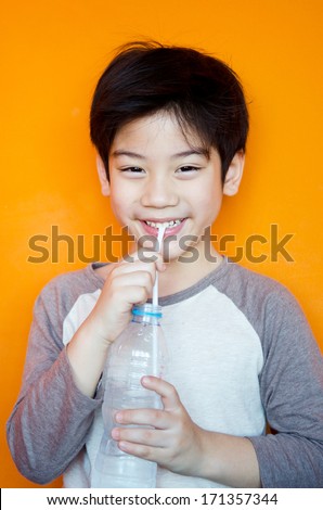 portrait of cute asian boy drinking water in bottle .