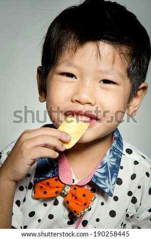 Portrait Of asian cute boy eating cookie on gray background .