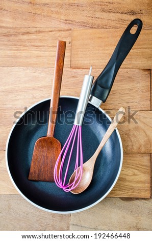 Closeup of  iron frying pan and wooden utensils on wood wall background .