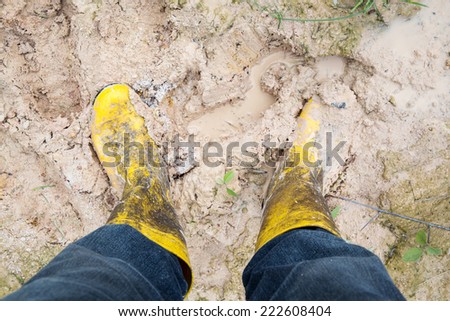 Human leg with Yelkow Muddy rubber boots on wet silt