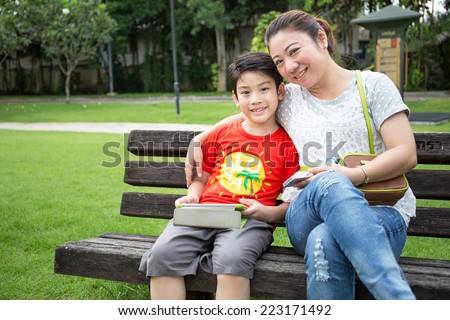 Asian woman and son with mobile phone and tablet computer in the park