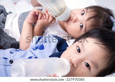 Closeup portrait of happy Asian little boy and girl are drinking milk from bottle on white background