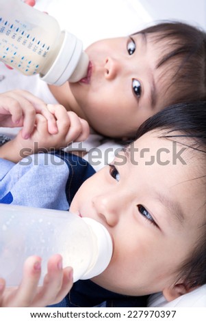Closeup portrait of happy Asian little boy and girl are drinking milk from bottle on white background