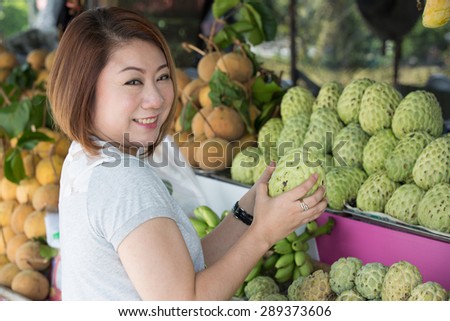 Happy asian woman choosing fresh custard apple fruit in the grocery shop on the foreground