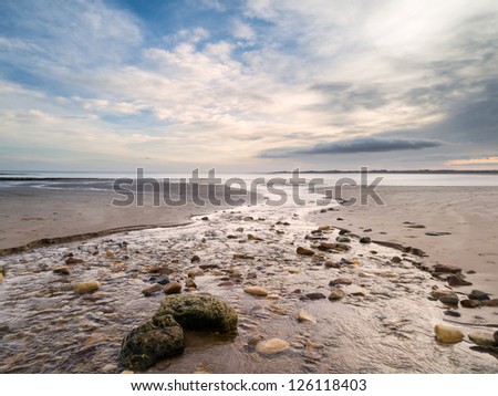 River winding across a flat deserted beach to the sea