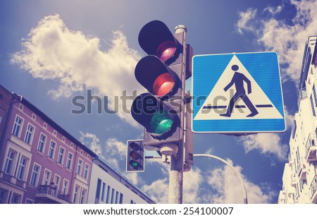 Retro filtered photo of traffic lights and pedestrian crossing sign in a city.