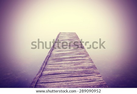 Vintage filtered picture of old wooden pier in dense fog with strong vignette effect.