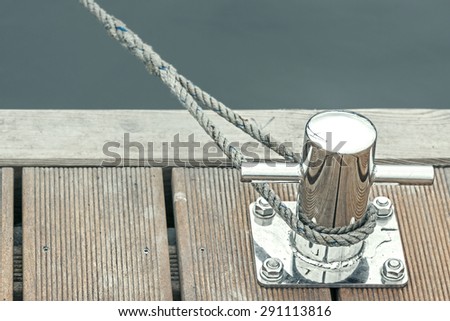 Blue toned marina bollard with rope, marine background with space for text.
