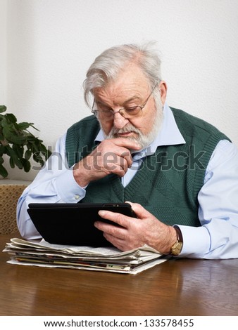 Senior man reading newspaper on digital tablet