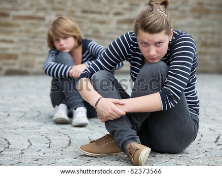 Teenage girls sitting on grounds, turned away from one another