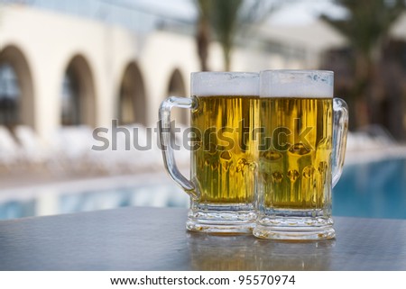Two beer mugs by swimming pool in tropical resort