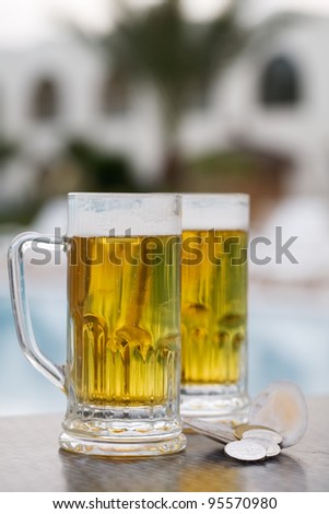 Two beer mugs and currency by swimming pool in tropical resort
