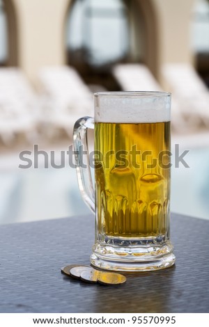 Beer mug and currency by swimming pool in tropical resort