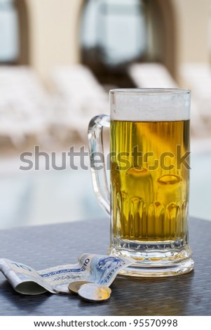 Beer mug and currency by swimming pool in tropical resort