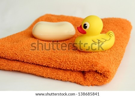 Set for bathing. Yellow rubber duck and white soap on orange towel. (Duck on focus)