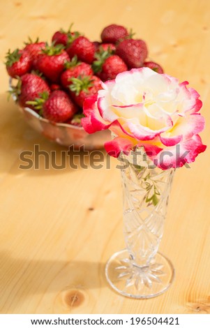 pink white rose in a glass vase, on wooden background and strawberry bowl