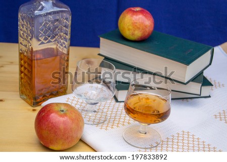 Glass and bottle of hard liquor like scotch, bourbon, whiskey or brandy on wood background with books and apples on white texture