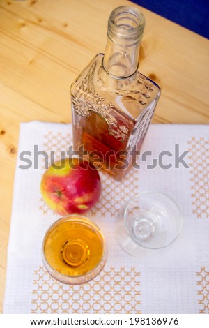 Glass and bottle of hard liquor like scotch, bourbon, whiskey or brandy on wood background and white texture and an apple