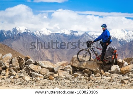 Happy mountain cyclist stands on a stone rock face in the high mountains. background blue sky with clouds, Himalayas, Indian Tibet