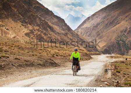 mountain bike rides along the winding dirt road in the high mountains. Background blue sky with clouds, Himalayas, Indian Tibet