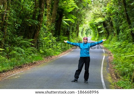 Girl standing with arms outstretched on the asphalt winding path outdoors in a green park of pure jungle , rain forest .
