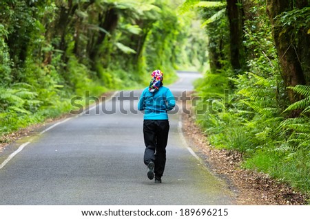 The girl runs on asphalt winding path outdoors in a green park of pure jungle , rain forest .
