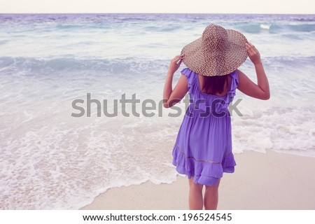 Woman running on the beach wearing a straw hat and a blue short dress. Vacation. vintage.