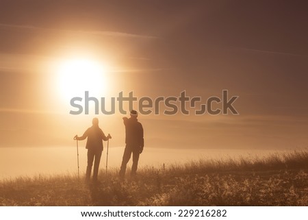 Silhouette active couple in love with Trekking pole in the morning fog. Landscape composition, background mountains and sunrise.