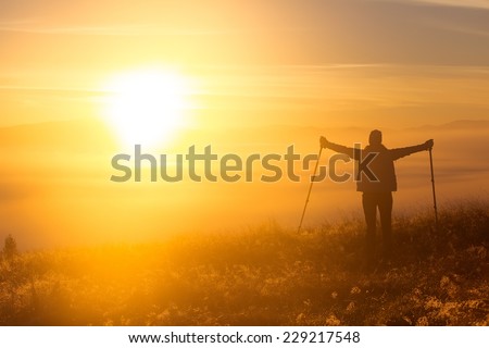 Silhouette of a girl with a lonely sport Trekking pole in the morning fog. Landscape composition, background mountains and sunrise.