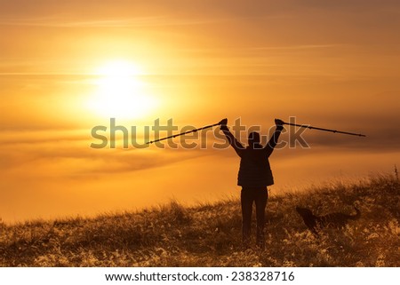 Silhouette of a girl with sports Trekking pole in the morning mist with a loyal friend, a dog. Landscape composition, background mountains and sunrise.