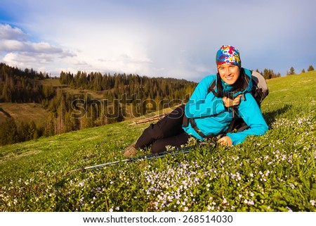 Healthy hiker girl in nature hike. Beautiful young woman hiking happy sits on a meadow. Background beautiful mountayns and blue sky with clouds