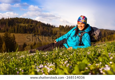 Healthy hiker girl in nature hike. Beautiful young woman hiking happy sits on a meadow. Background beautiful mountayns and blue sky with clouds
