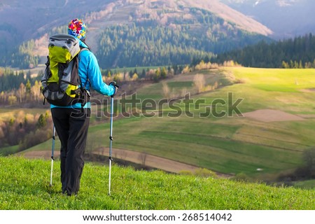 Healthy hiker girl in nature hike. Beautiful young woman hiking happy with Trekking pole stands on a meadow. Background beautiful mountayns and blue sky with clouds
